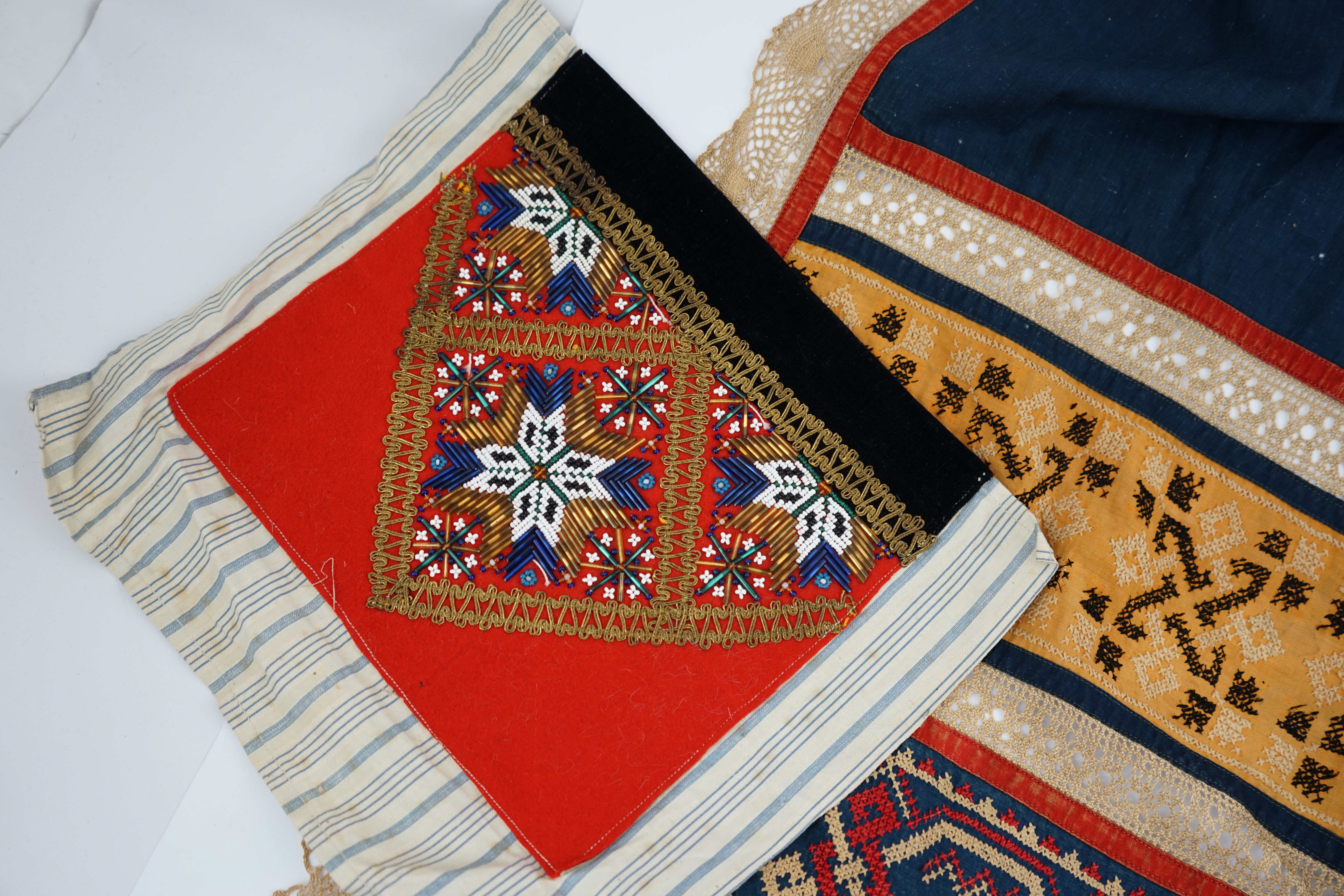 An Eastern European, possibly Ukrainian, apron and a Norwegian beaded bodice front, with child’s cap, the apron worked in rows of coloured cotton, embroidered with cross stitch patterns and lace insertions, the bodice, b